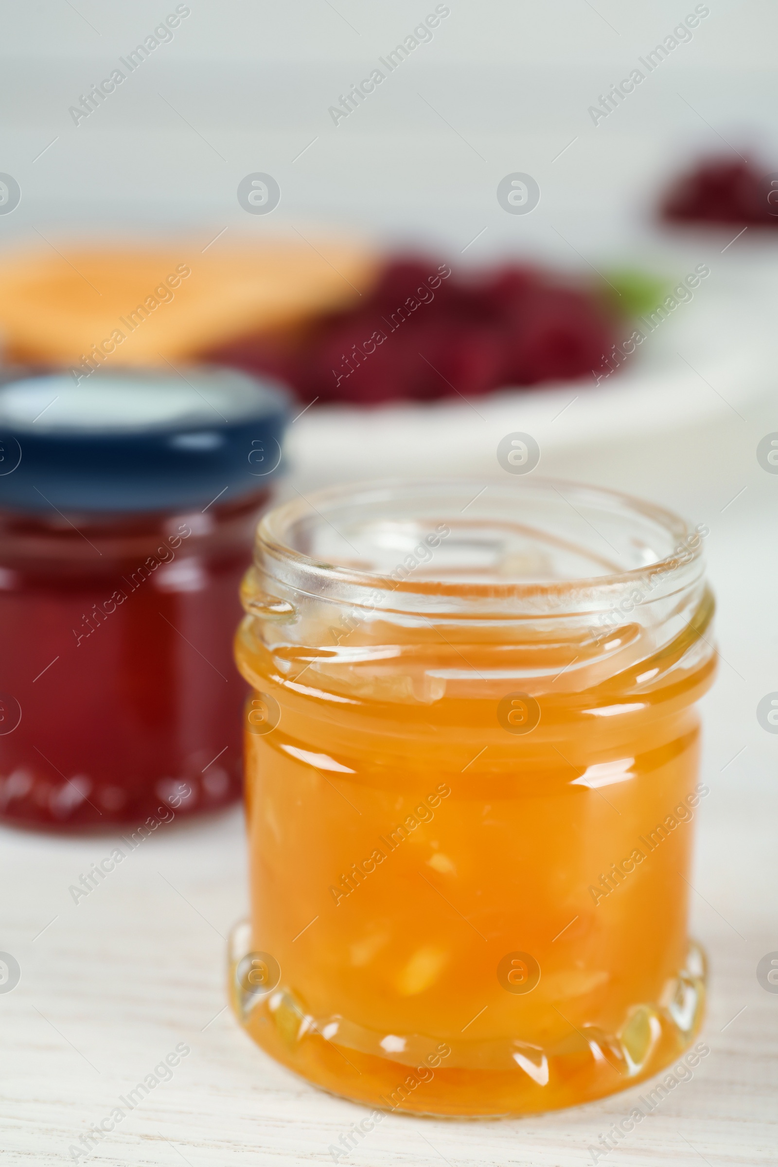 Photo of Open glass jar of sweet jam on white wooden table, closeup. Space for text