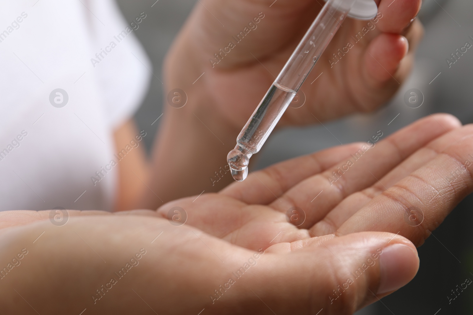 Photo of Woman applying cosmetic serum onto her hand on blurred background, closeup