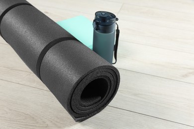 Photo of Exercise mat, yoga block and bottle of water on light wooden floor, closeup. Space for text
