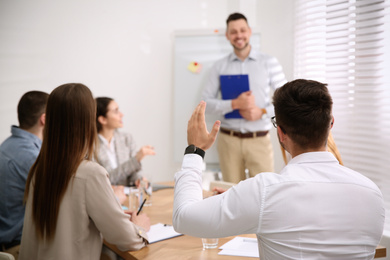 Photo of Young man raising hand to ask question at business training in conference room