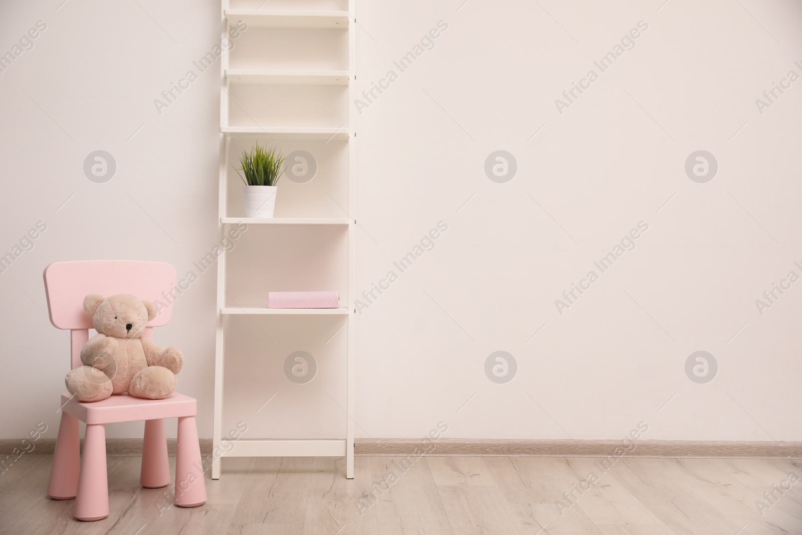 Photo of Teddy bear on chair and shelving unit near wall in child room. Space for text