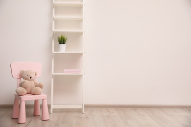 Teddy bear on chair and shelving unit near wall in child room. Space for text