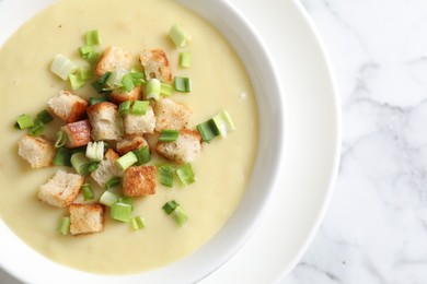 Photo of Tasty potato soup with croutons and green onion in bowl on white marble table, top view