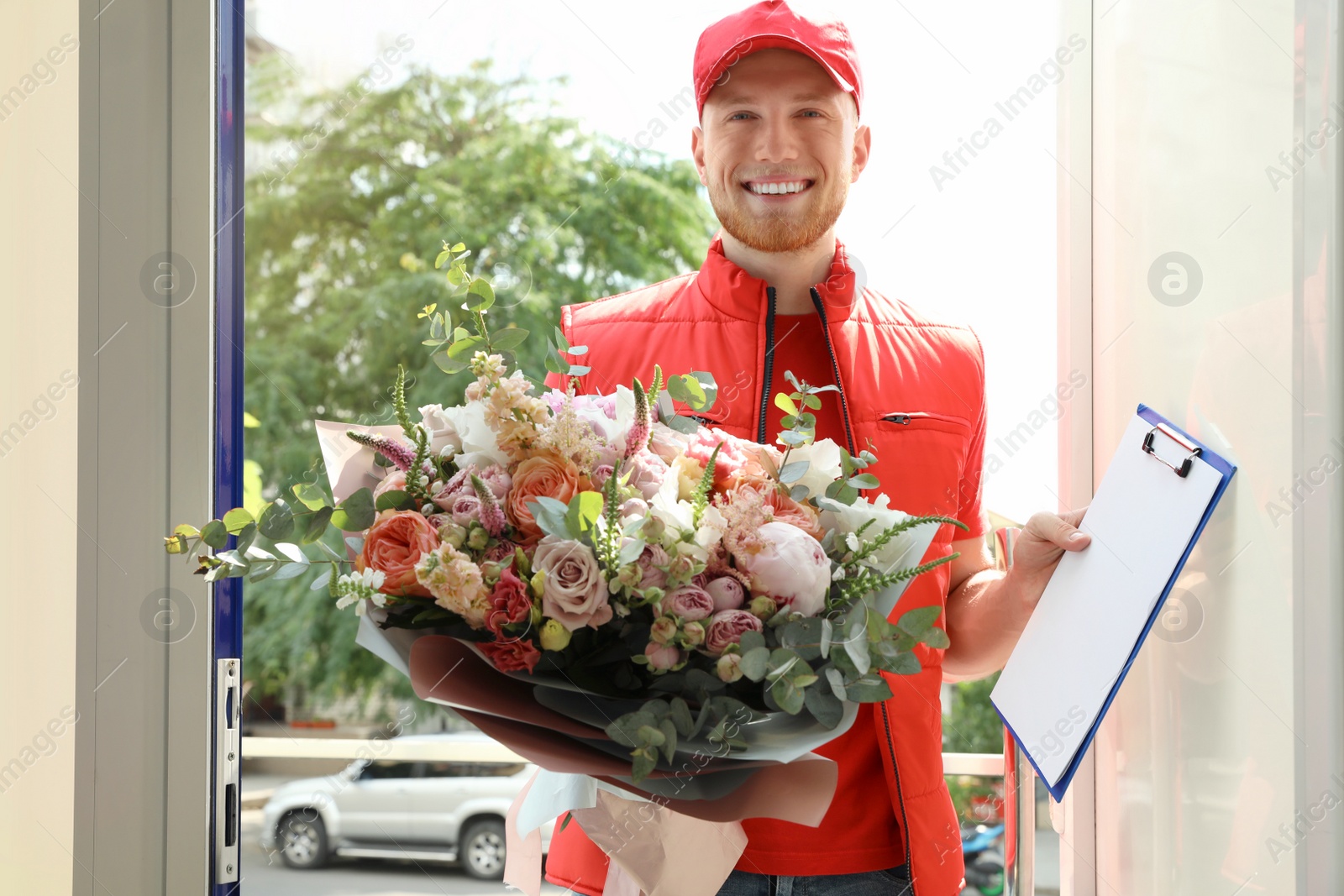 Photo of Delivery man with beautiful flower bouquet and clipboard in doorway