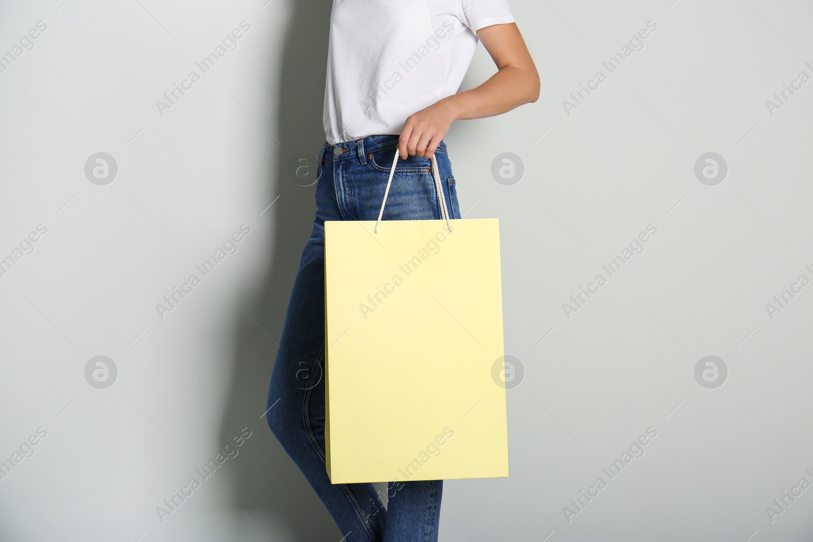 Photo of Woman with paper shopping bag on light grey background, closeup