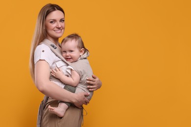 Mother holding her child in sling (baby carrier) on orange background. Space for text