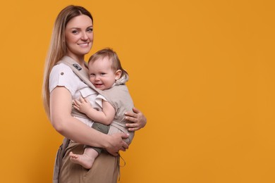 Photo of Mother holding her child in sling (baby carrier) on orange background. Space for text