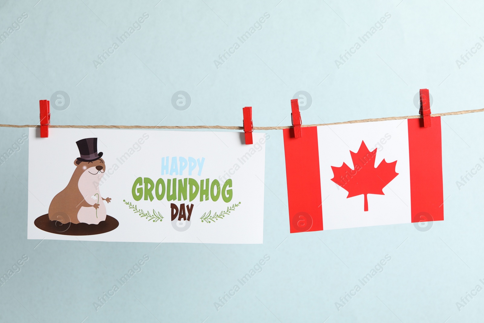 Photo of Happy Groundhog Day greeting card and Canada flag hanging against light background