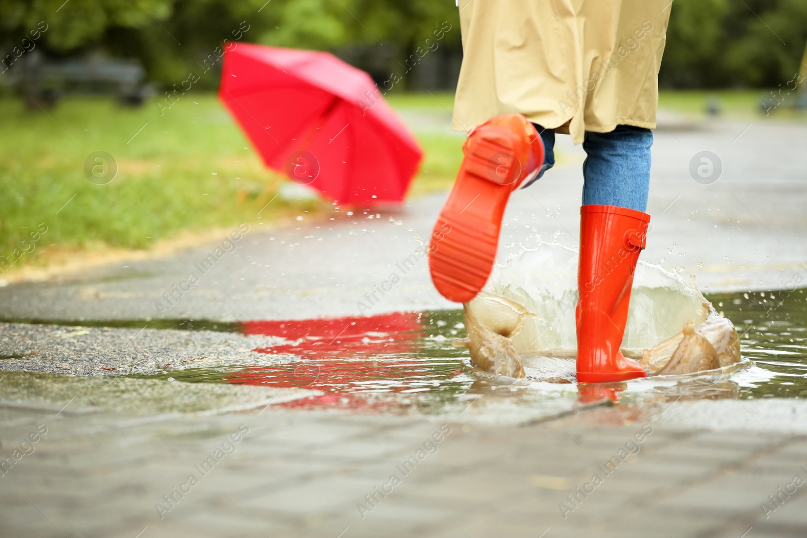Photo of Woman in red rubber boots running after umbrella on street, closeup. Rainy weather