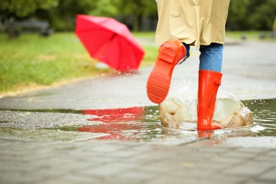 Woman in red rubber boots running after umbrella on street, closeup. Rainy weather