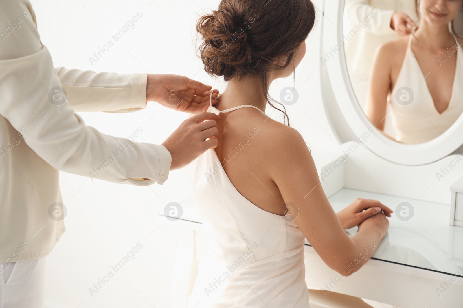 Photo of Woman helping bride to get ready for her wedding indoors, closeup