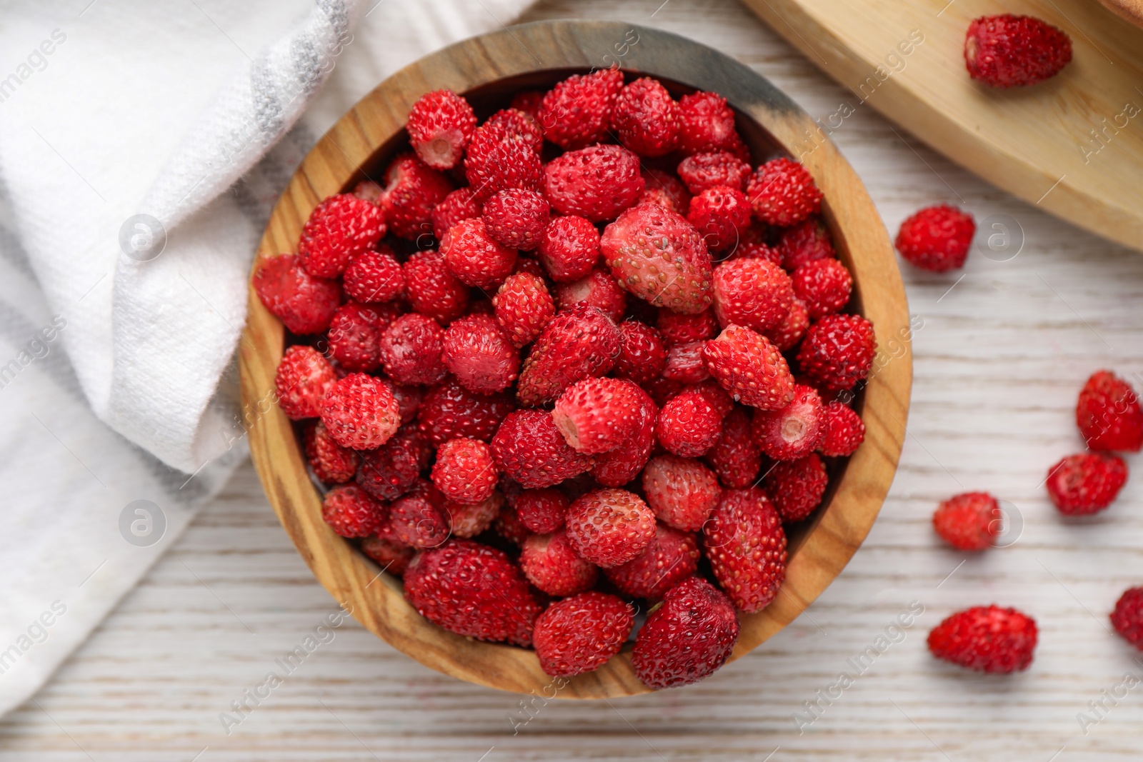 Photo of Fresh wild strawberries in bowl on white wooden table, flat lay