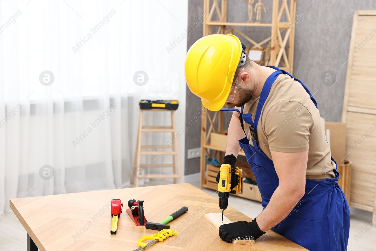 Photo of Young worker using electric drill at table in workshop