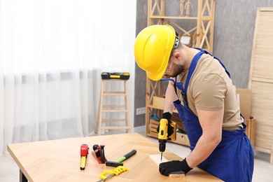 Photo of Young worker using electric drill at table in workshop