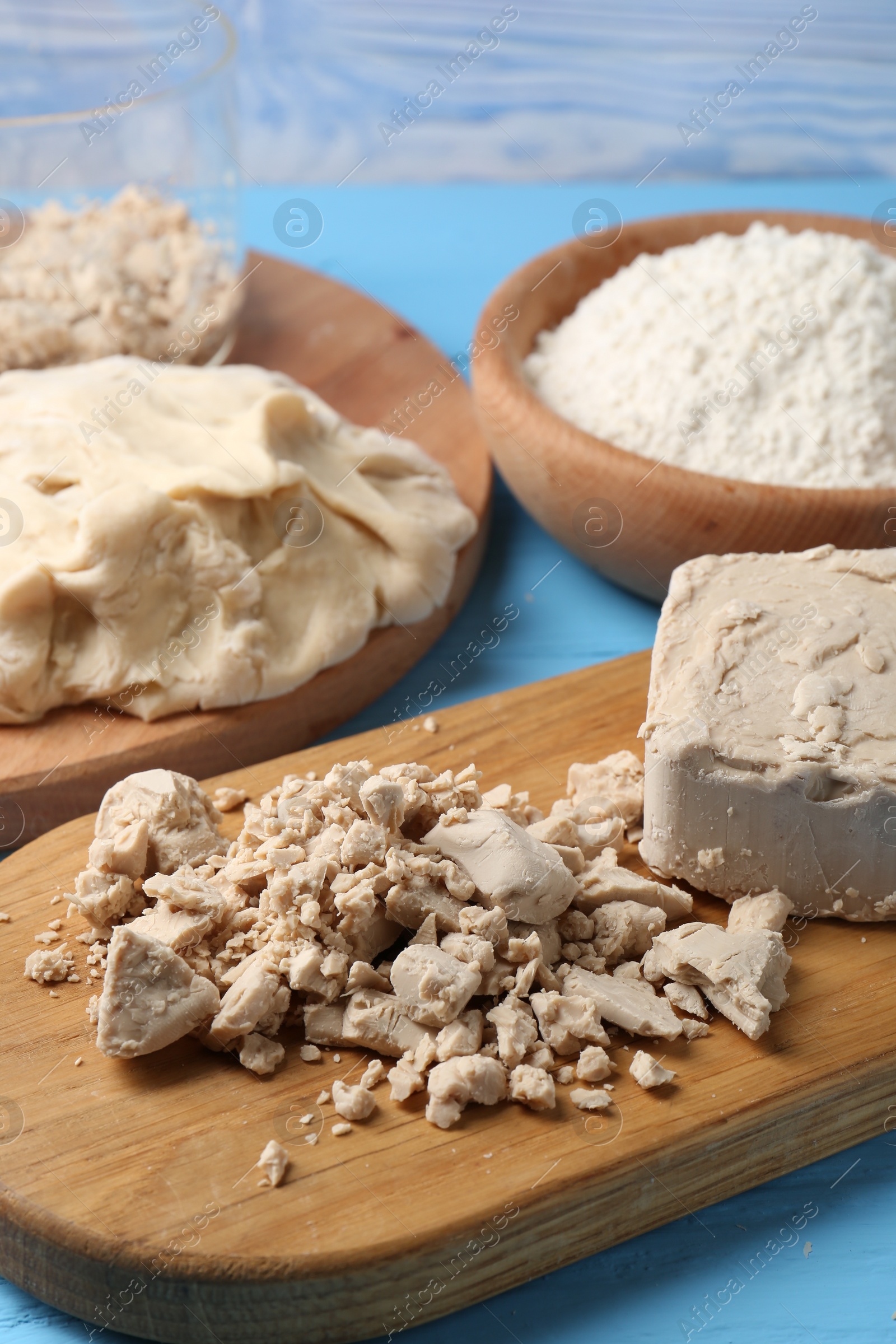 Photo of Compressed yeast, dough and flour on light blue wooden table, closeup