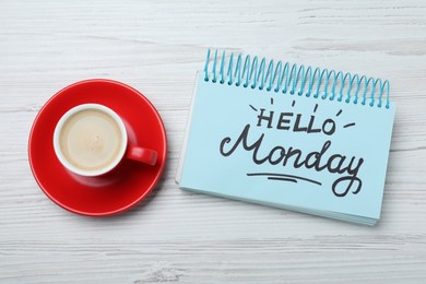 Message Hello Monday written in notebook and cup of coffee on white wooden desk, flat lay