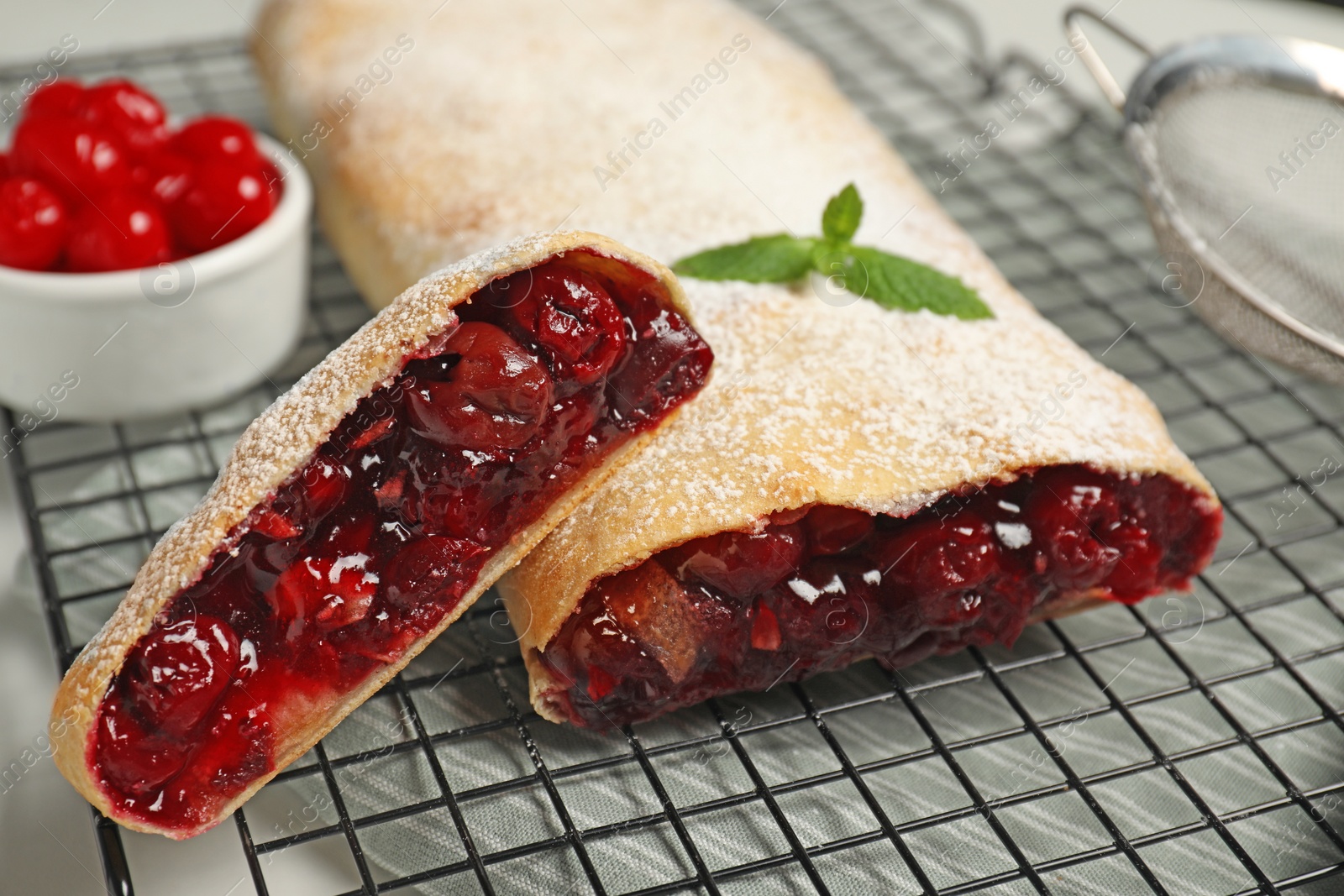Photo of Delicious strudel with cherries on cooling rack, closeup