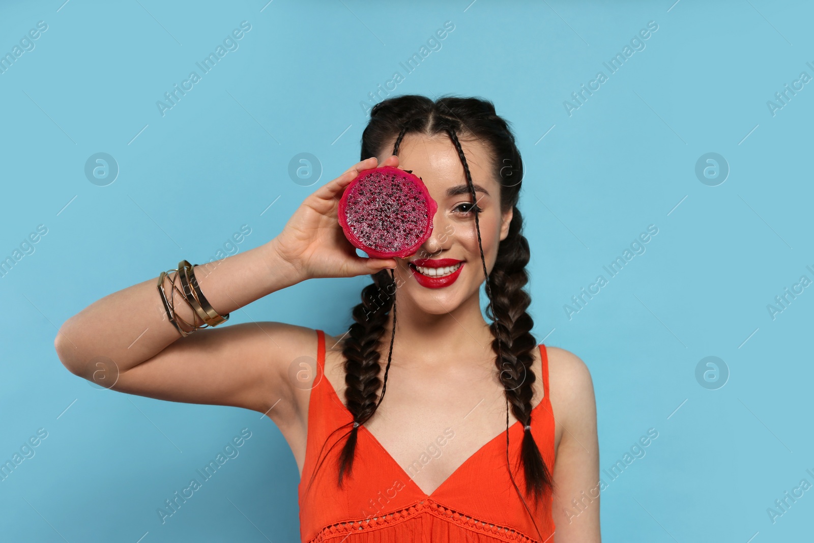 Photo of Young woman with fresh pitahaya on light blue background. Exotic fruit