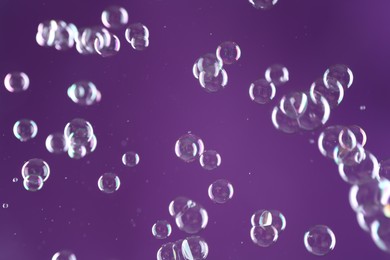 Photo of Beautiful transparent soap bubbles on purple background