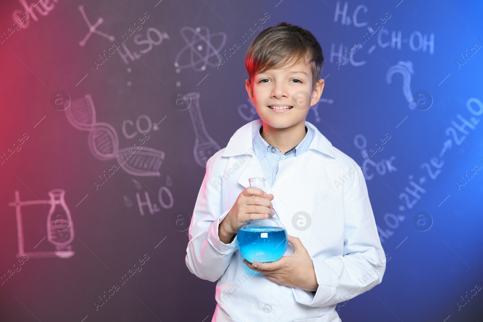Photo of Schoolboy holding Florence flask against blackboard with written chemistry formulas. Space for text