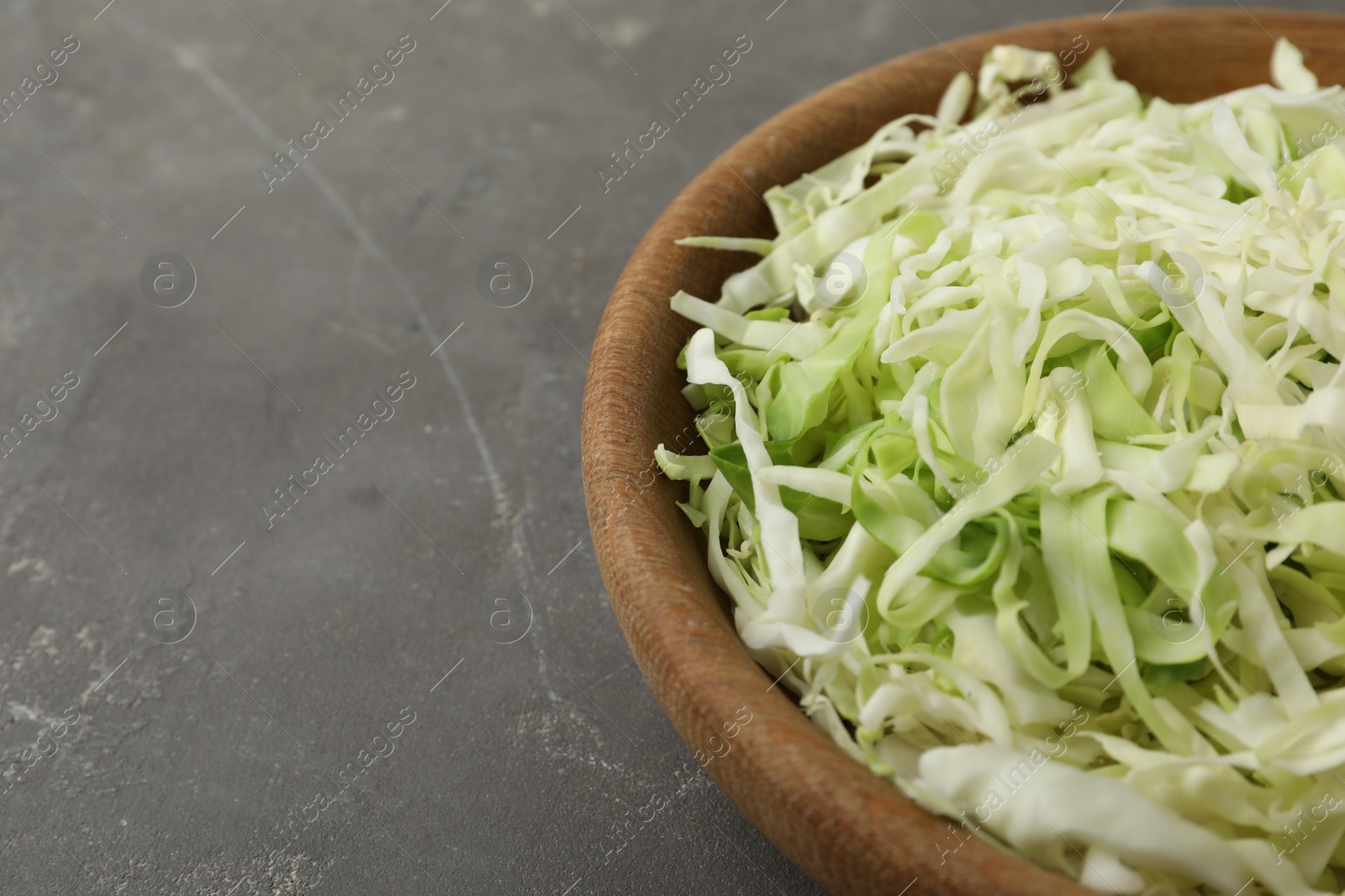 Photo of Chopped cabbage in bowl on grey table, closeup. Space for text