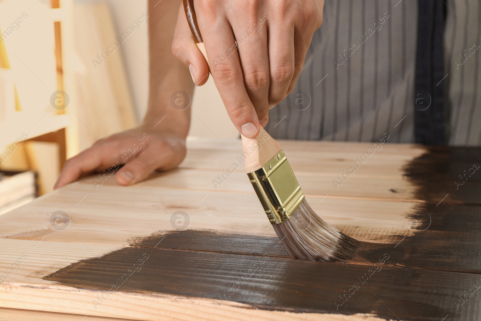 Photo of Man with brush applying wood stain onto wooden surface indoors, closeup