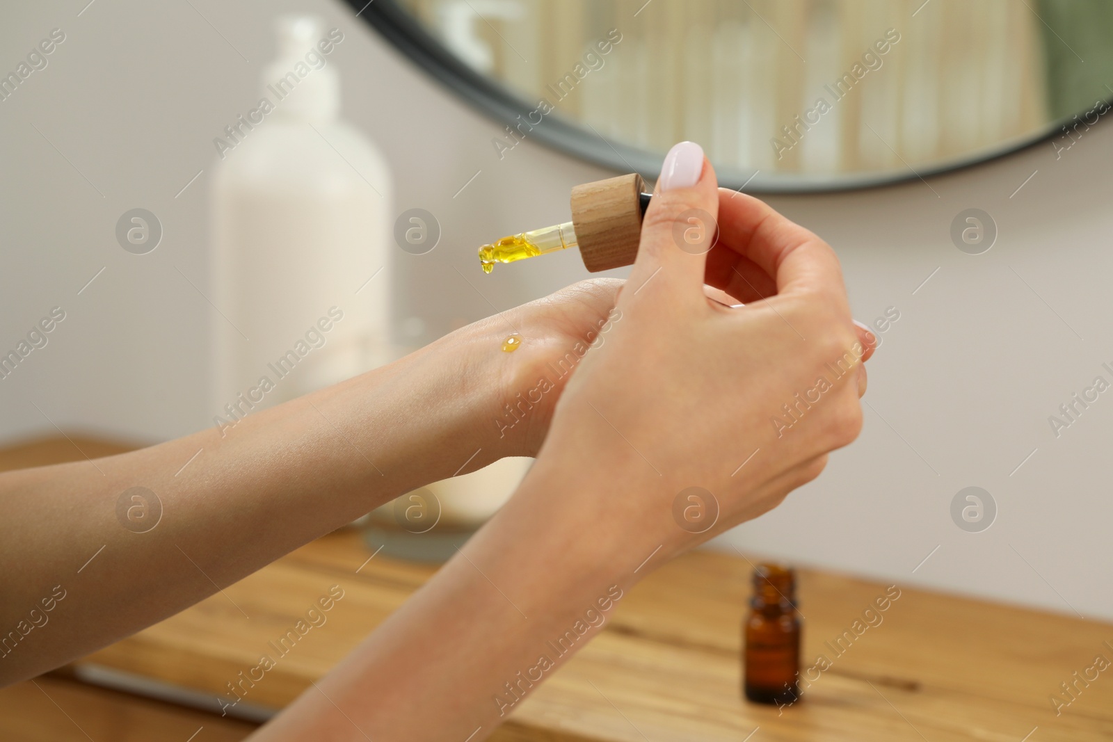 Photo of Young woman applying essential oil on wrist indoors, closeup