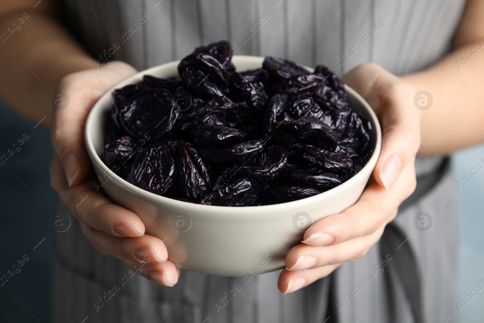 Photo of Woman holding bowl of dried plums, closeup. Healthy fruit