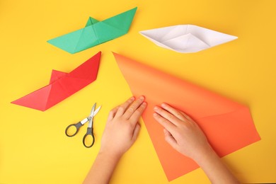 Photo of Origami art. Child folding paper on yellow background, closeup and top view