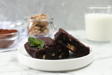 Photo of Delicious brownies with nuts and mint on white marble table