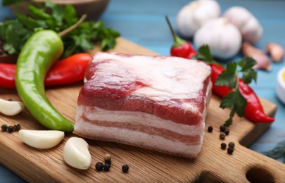 Photo of Piece of pork fatback with garlic and chilli pepper on wooden board, closeup