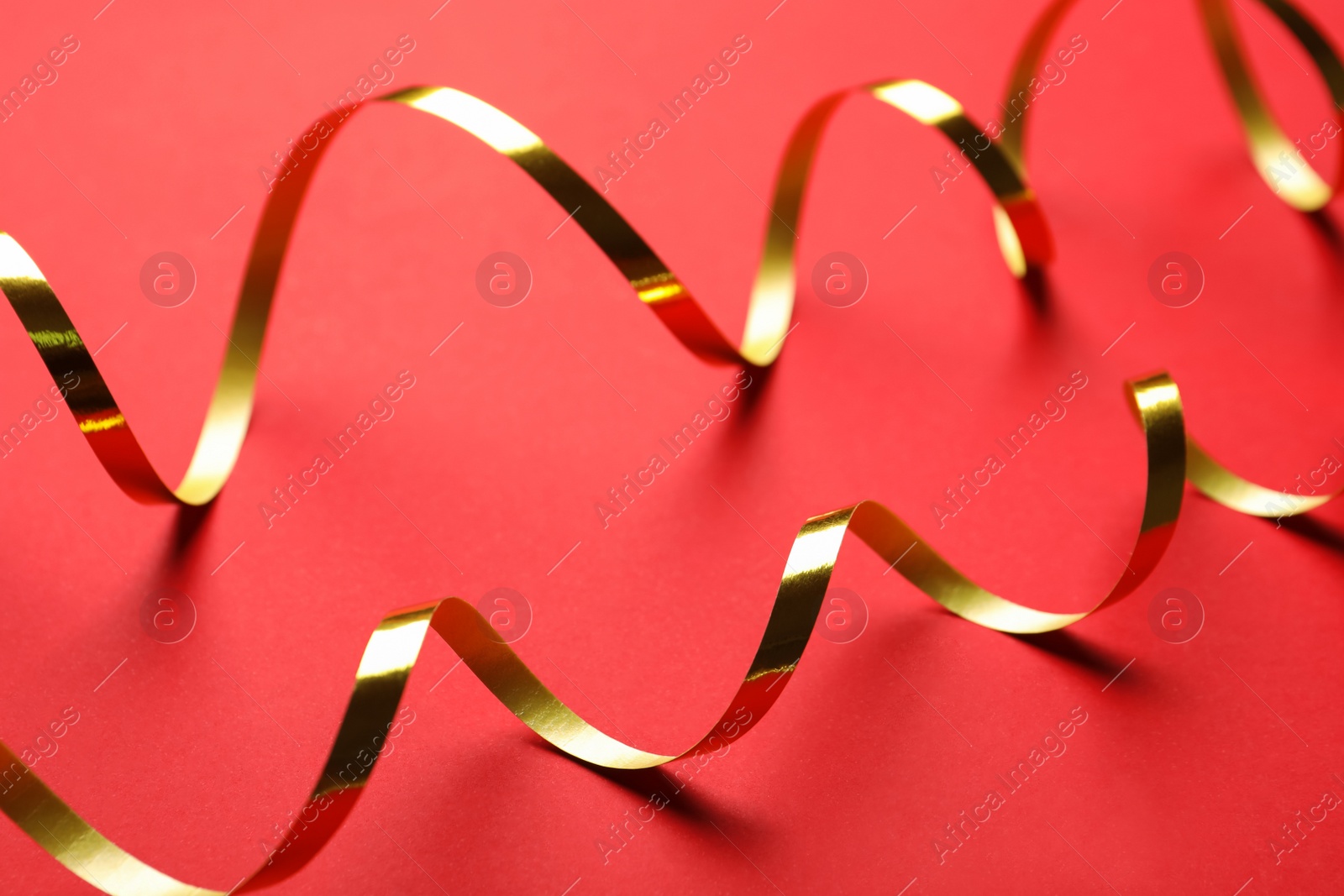 Photo of Shiny golden serpentine streamers on red background, closeup