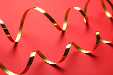 Shiny golden serpentine streamers on red background, closeup