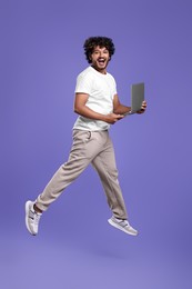 Photo of Happy man with laptop jumping on purple background