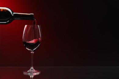 Photo of Pouring red wine from bottle into glass on dark background, space for text