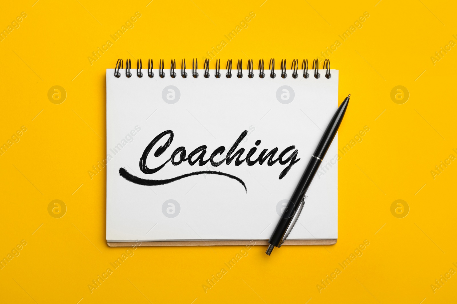 Image of Adult learning. Open notebook with word Coaching and pen on yellow background, top view