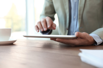 Photo of Businessman working with modern tablet at wooden table in office, closeup