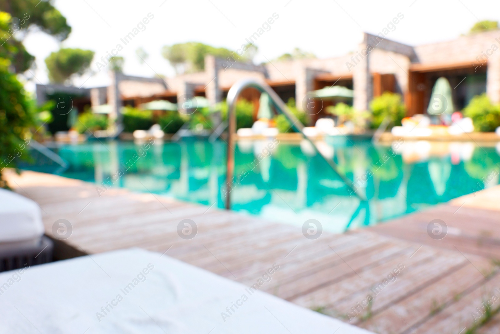 Photo of Outdoor swimming pool with wooden deck and sun loungers, blurred view. Luxury resort