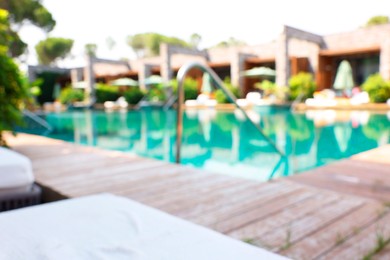 Photo of Outdoor swimming pool with wooden deck and sun loungers, blurred view. Luxury resort