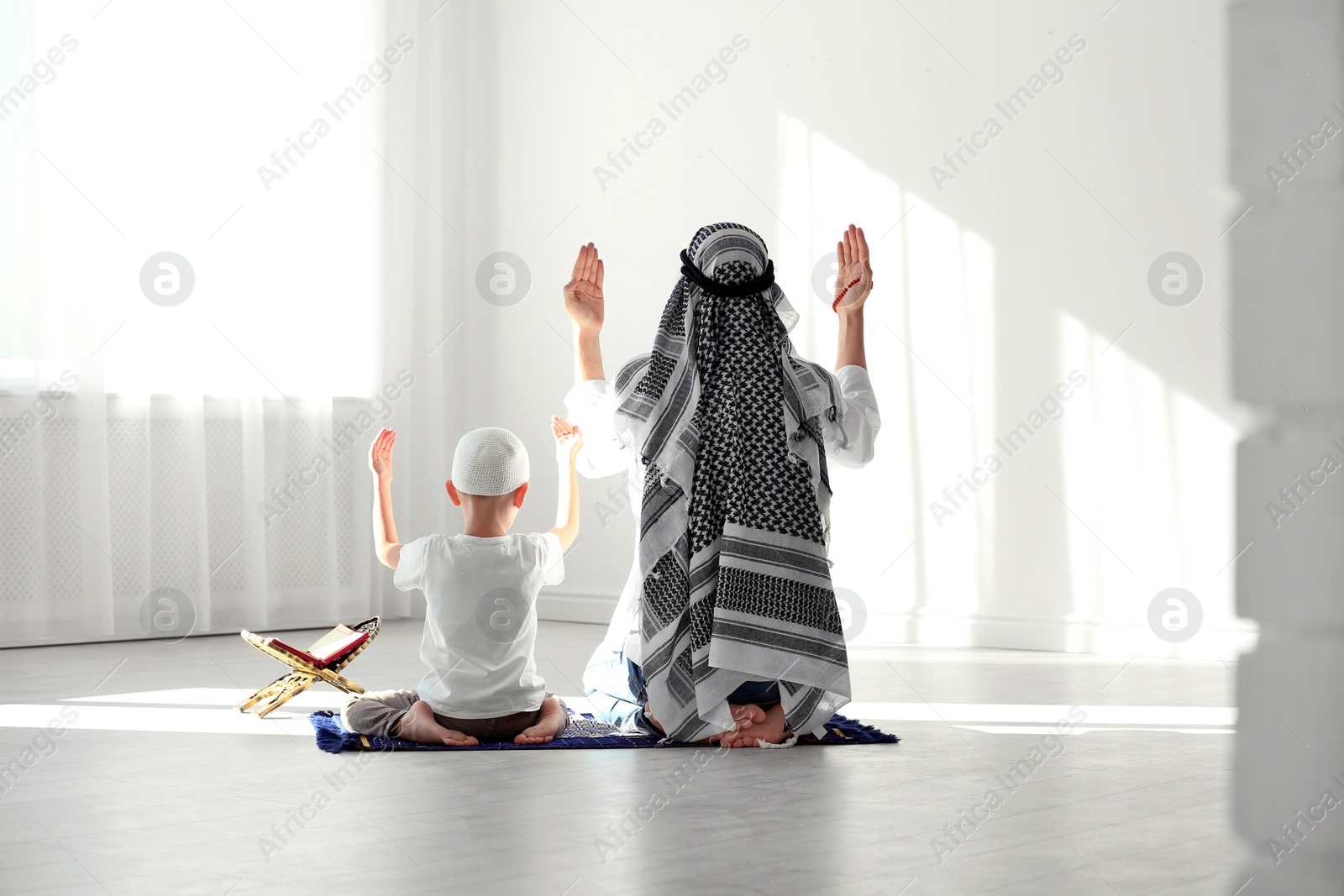 Photo of Muslim man and his son praying together indoors