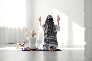 Photo of Muslim man and his son praying together indoors