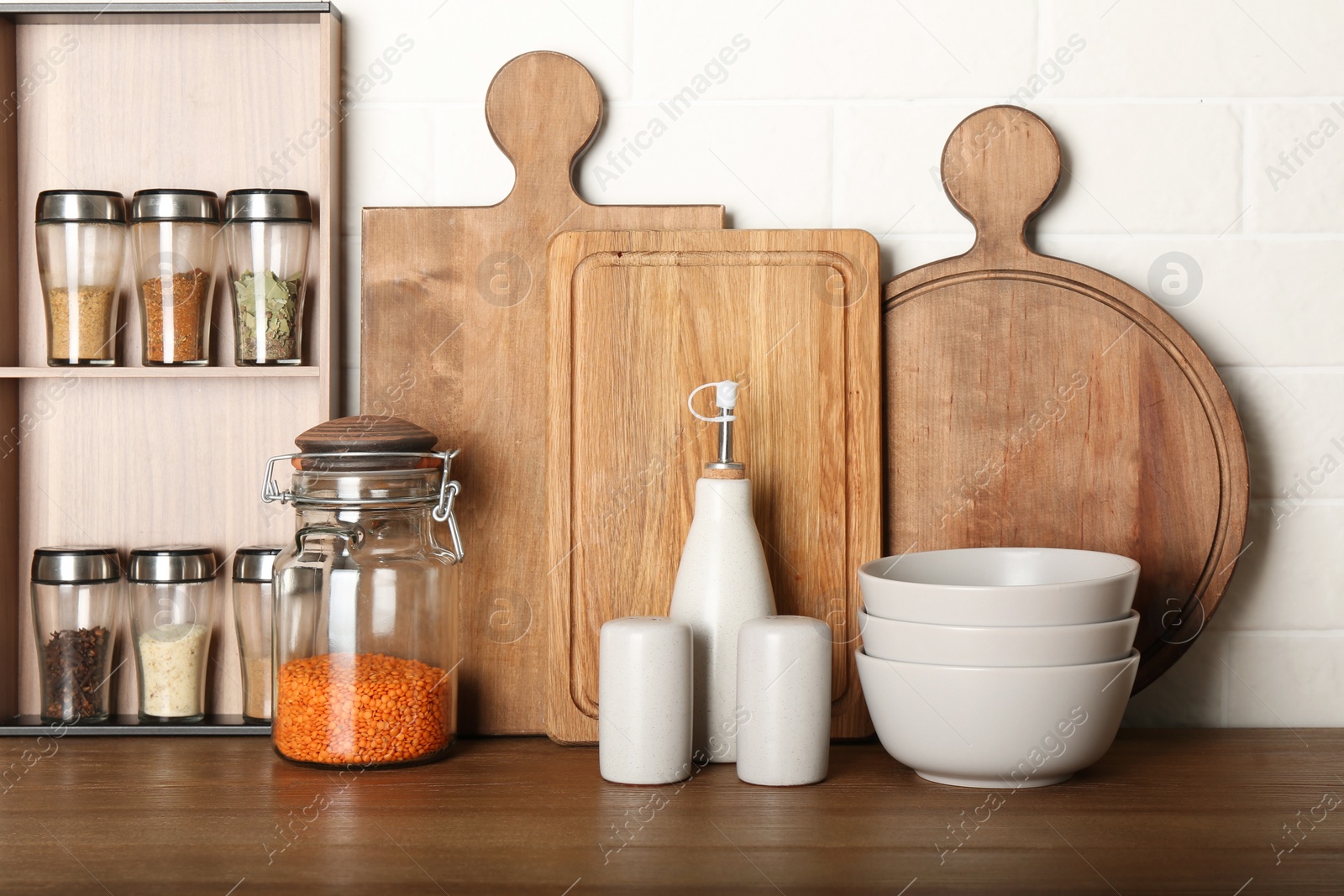 Photo of Set of spices and different dishware on wooden table near white brick wall in kitchen