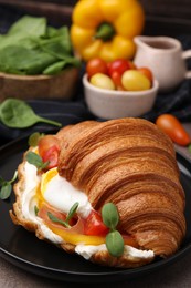 Photo of Tasty croissant with fried egg, tomato and microgreens on brown table, closeup