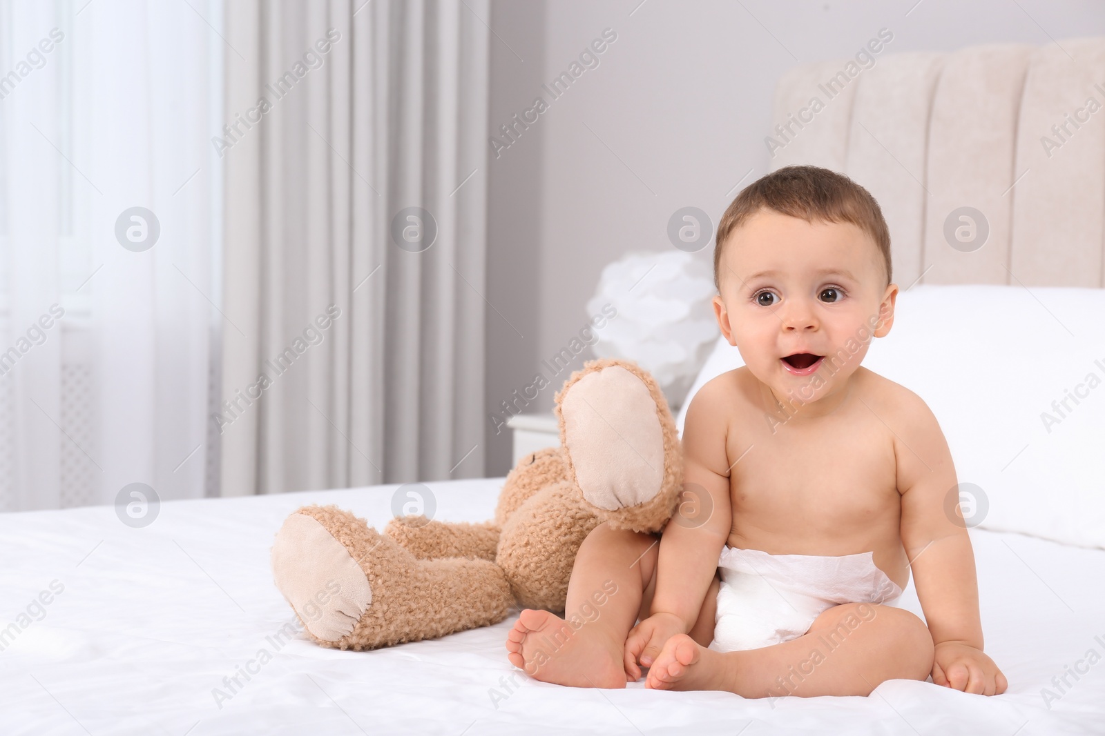 Photo of Cute baby in dry soft diaper with toy on white bed at home