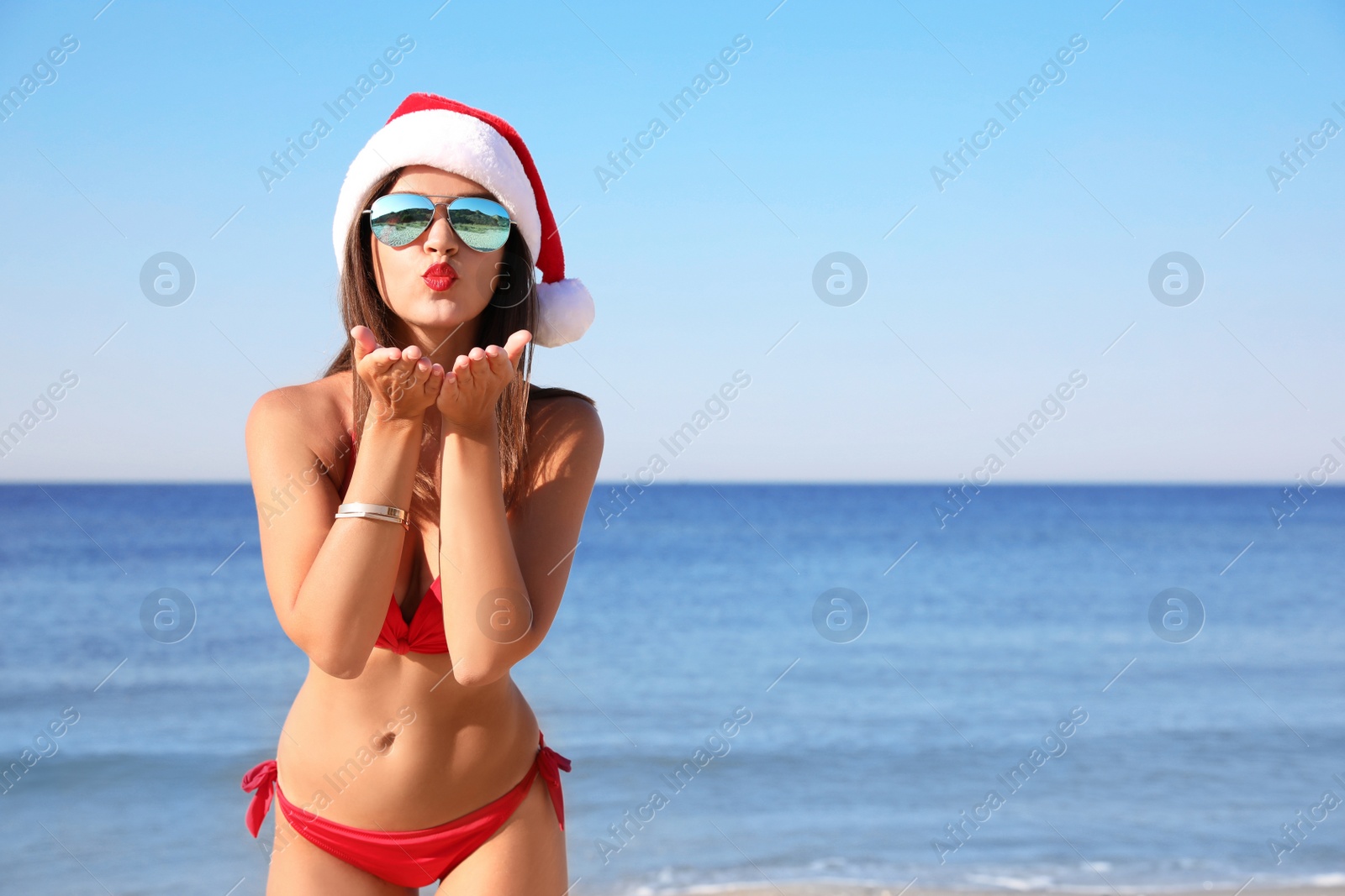 Photo of Young woman wearing Santa hat and bikini on beach, space for text. Christmas vacation