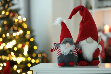 Photo of Funny Christmas gnomes on table in room with festive decoration. Space for text