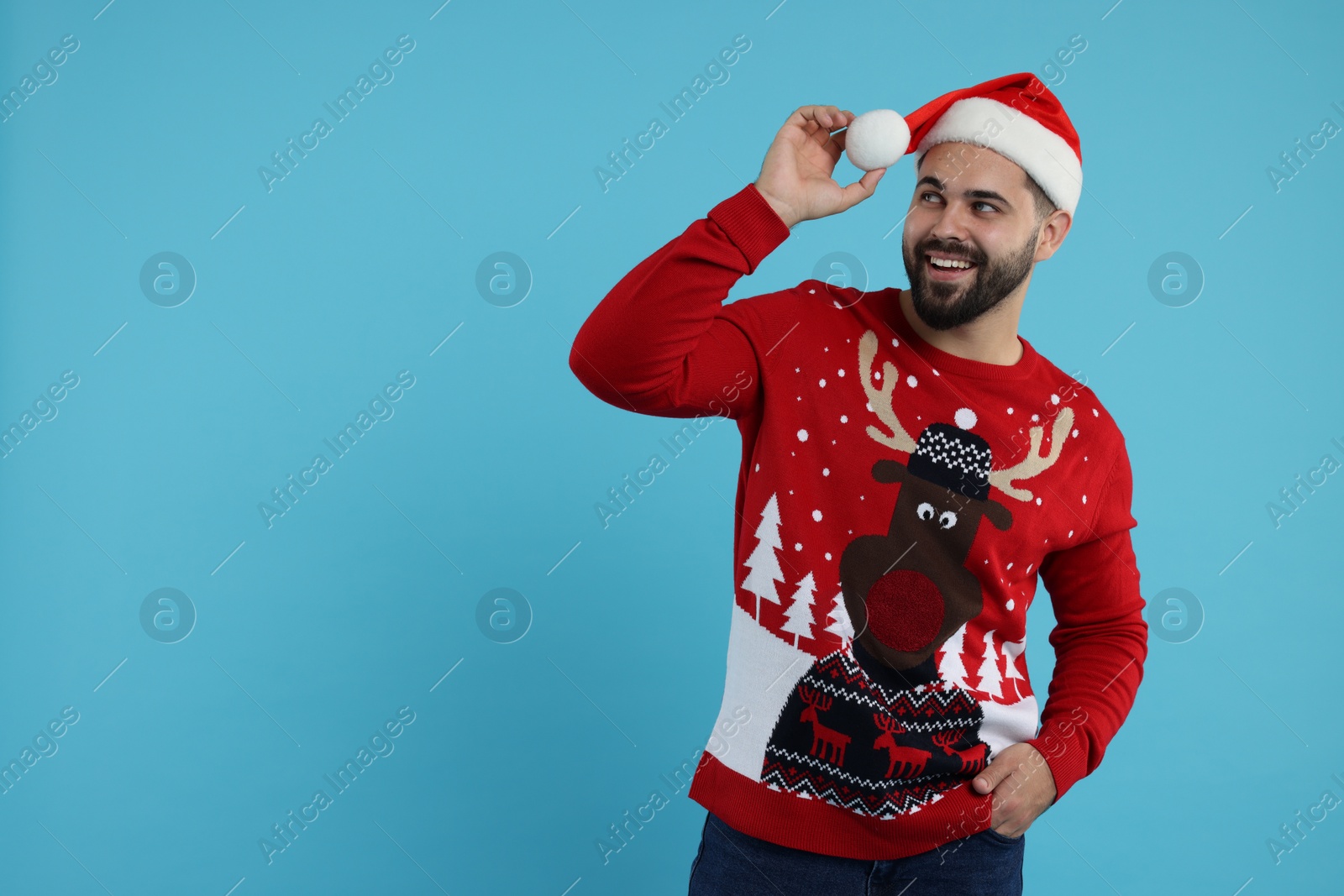 Photo of Happy young man in Christmas sweater and Santa hat on light blue background. Space for text