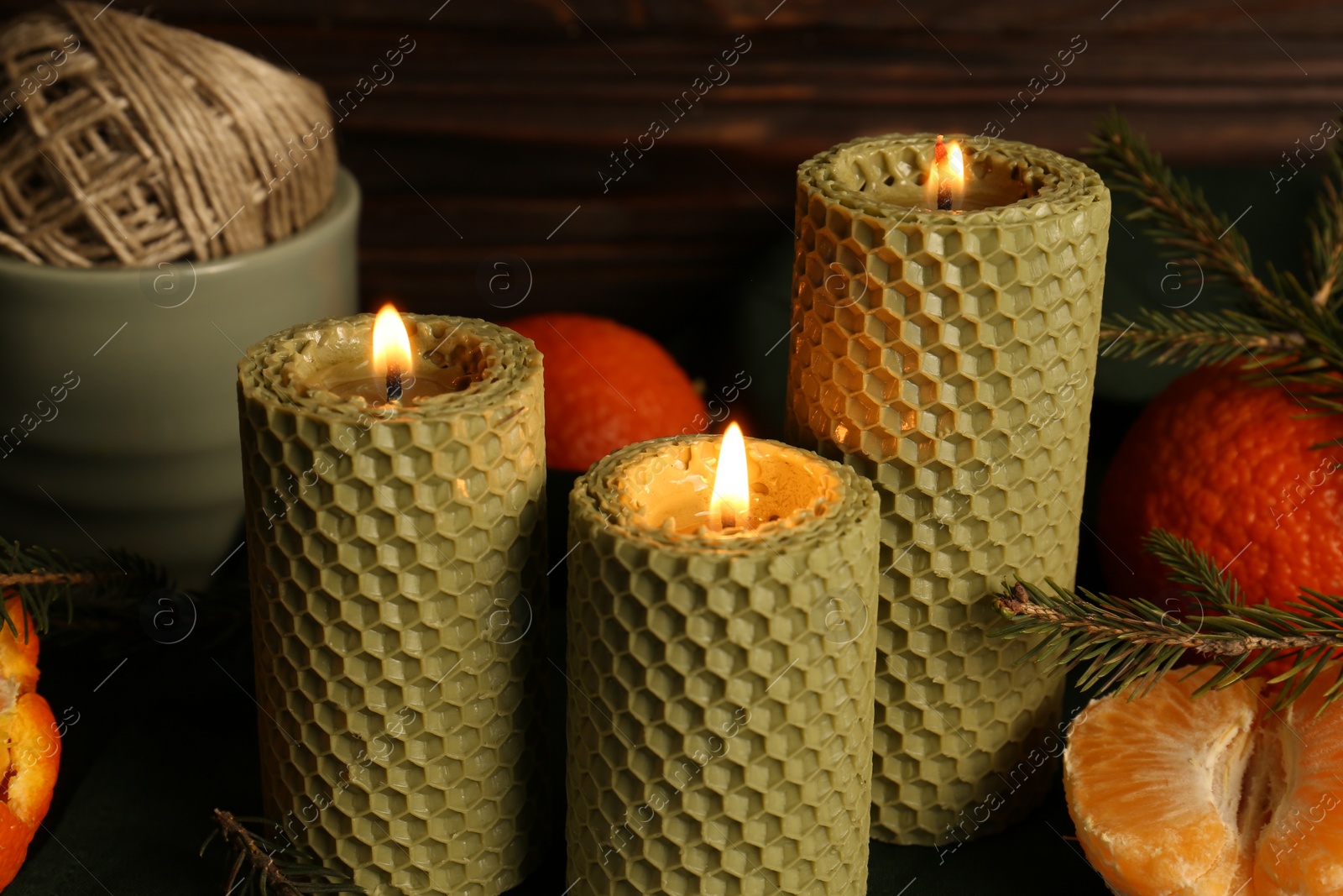 Photo of Beautiful burning beeswax candles, spruce twigs and tangerines on table, closeup