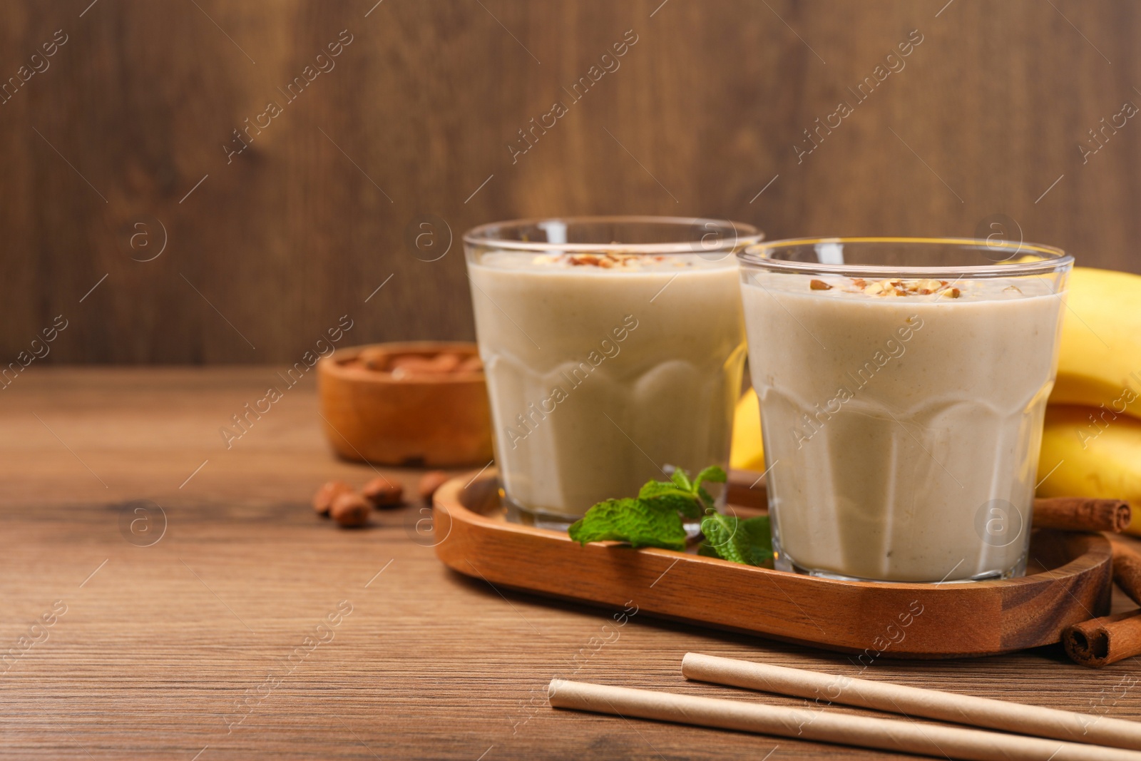 Photo of Tasty banana smoothie with almond and cinnamon on wooden table. Space for text