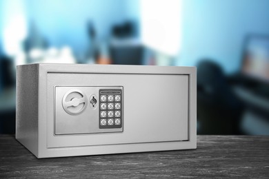 Image of Closed steel safe with electronic lock on grey wooden table indoors